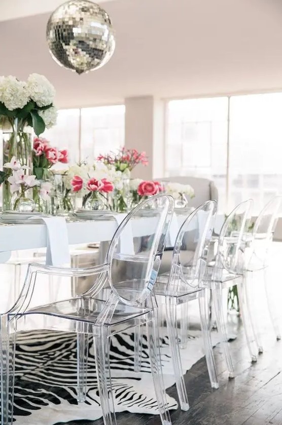 a glam dining space with a white table, ghost chairs, an animal print rug, a disco ball and bold blooms
