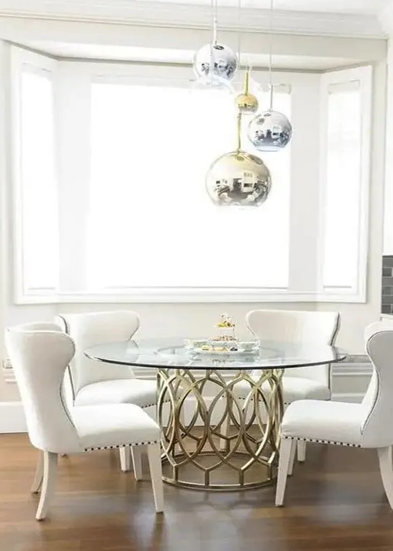 a glam dining space with metallic sphere pendant lamps, a brass table base and a round tabletop, comfy cream chairs