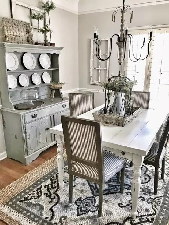 a greyish living room with a whitewashed buffet, a white table, striped chairs and a vintage chandelier