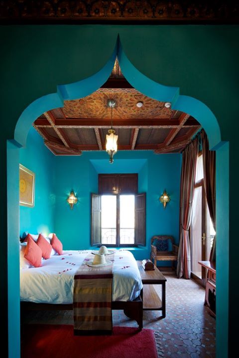 a jaw dropping Moroccan turquoise bedroom with a large bed, a stained bench and carved furniture plus a gorgeous ceiling