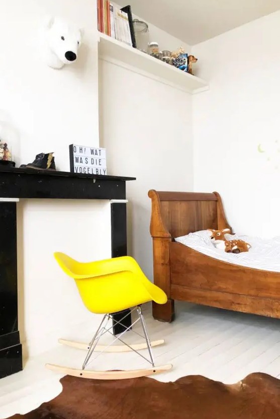 a kid's room with a faux fireplace, a stained bed, a yellow Eames rocker, a couple of shelves and toys