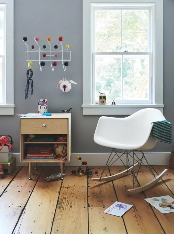 a kids' space with a stained cabinet, a white rocking chair, some toys, a rack and kids' drawings