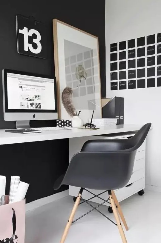 a laconic Nordic home office with a black statement wall and Eames chair, a black noteboard, a white desk and a relaxed artwork