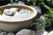 a large porcelain bowl with rocks and a single bloom, with rocks and pebbles around is a cool and modern decor idea