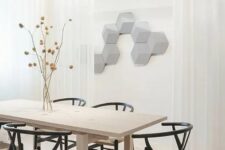 a light-colored modern dining space with a light-stained table, black wishbone chairs, dried blooms, hexagon panels