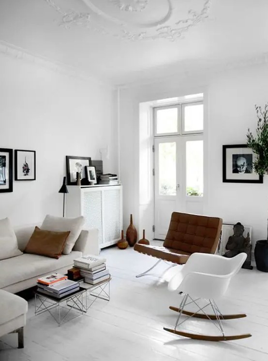 a light filled Scandinavian living room with a neutral sofa, a couple of coffee tables, a white Eames rocking chair, a leather one and some artwork