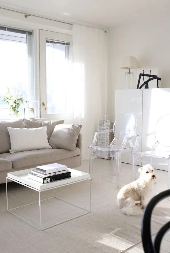 a light filled living room with a greige sofa, a white coffee table, ghost chairs, a white storage cabinet and black touches