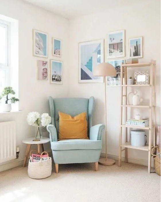 a light-filled nook with a blue Strandmon chair, a side table, a light-stained shelving unit, a gallery wall on two walls
