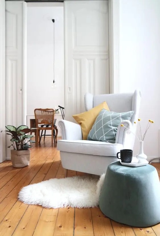 a light-filled space with a Strandmon chair, a pale blue pouf, pillows, a faux fur rug and a potted plant is amazing