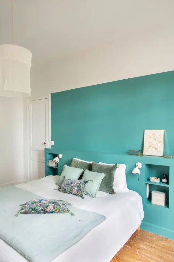 a lovely contemporary bedroom with a turquoise accent wall and storage niches, a bed with light green and neutral bedding and a pendant lamp