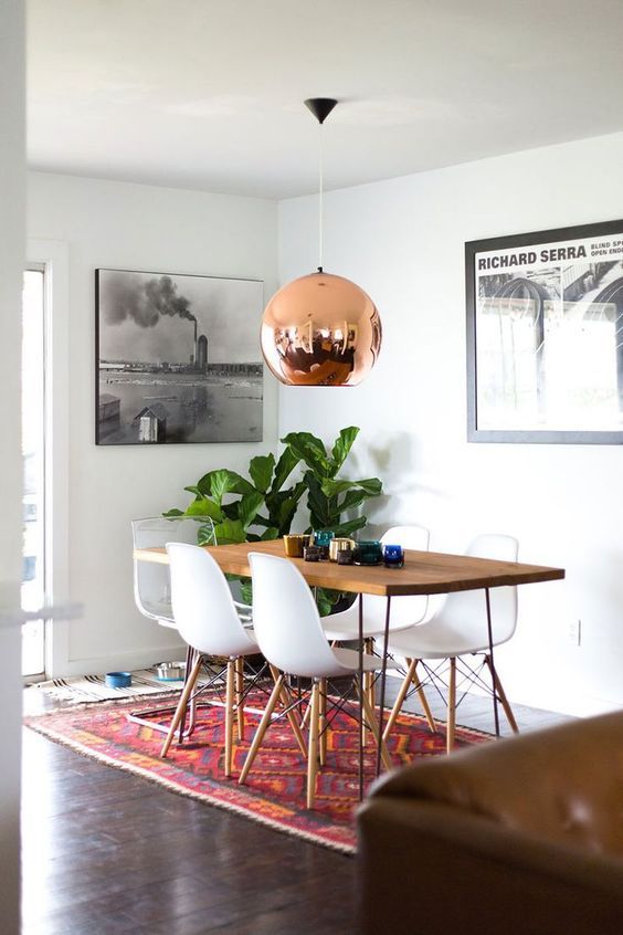 a mid-century modern dining space with a stained table, white Eames chairs, a copper pendant lamp and some artwork
