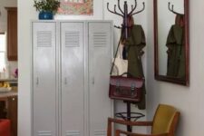 a mid-century modern mudroom with grey lockers, a mustard chair, a mirror in a dark-stained frame, a rack and some bright decor