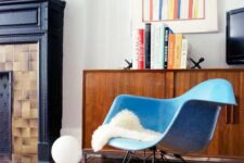 a mid-century modern nook with a stained credenza, a blue Eames rocking chair, a non-working fireplace, bold decor and books