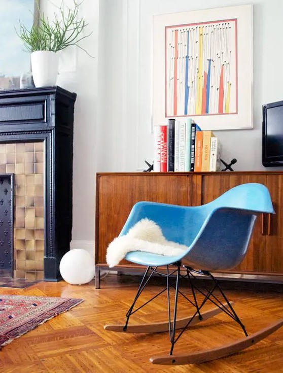 a mid century modern nook with a stained credenza, a blue Eames rocking chair, a non working fireplace, bold decor and books
