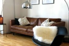 a minimal living room with a brown leather sofa, a black Eames rocking chair, some pillows, a floor lamp and a gallery wall