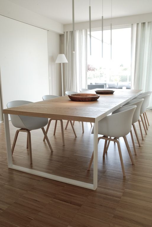 a minimal neutral dining space with a stained table, white chairs, white pendant lamps shaped as tubes