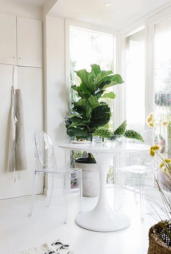 a minimalist and light-filled breakfast nook with a round table, ghost chairs, potted plants and a view of the garden