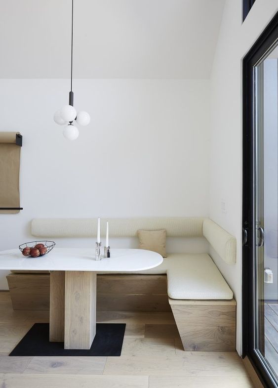 a minimalist corner dining space with a corner upholstered bench, an oval table, a catchy pendant lamp