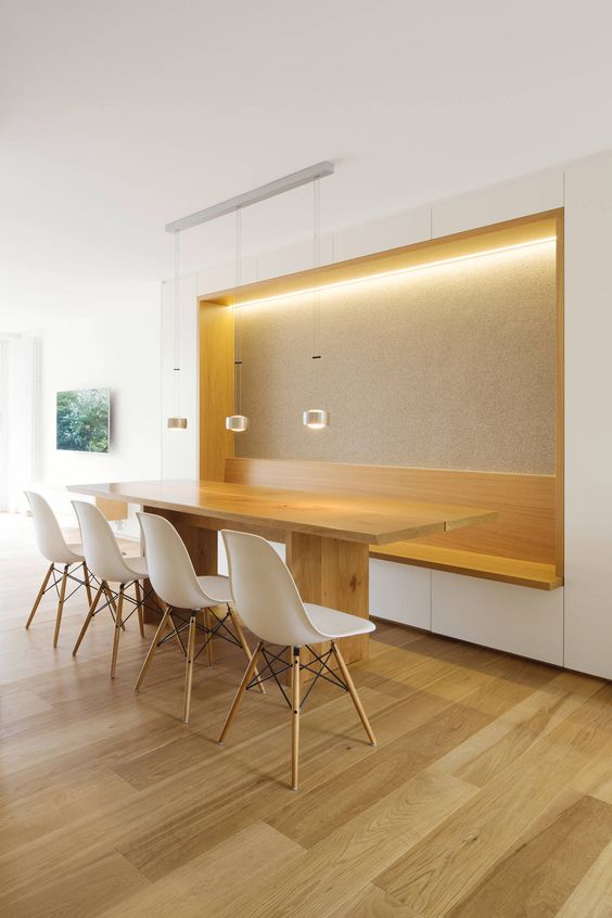 a minimalist dining room with a built in bench with lights, a stained table and white chairs and pendant lamps over the table