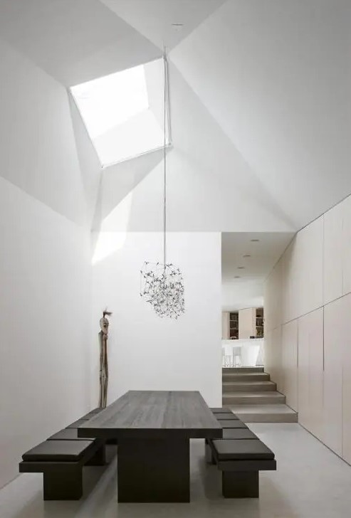 a minimalist dining room with a plywood accent wall, a black table and benches, a skylight and catchy burst chandeliers