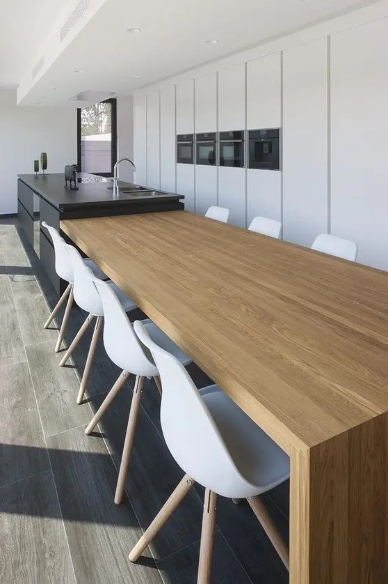 a minimalist dining room with a stained table that is attached to the kitchen island, and white Eames chairs