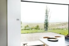 a minimalist dining space with a glazed wall to enjoy the views, a large table and chairs and stools and nothing else