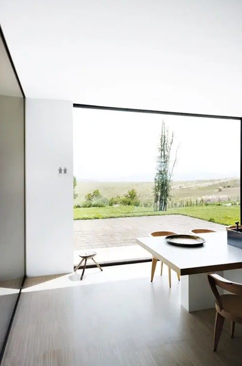 a minimalist dining space with a glazed wall to enjoy the views, a large table and chairs and stools and nothing else