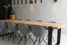a minimalist dining space with a long light-stained table, grey chairs, a cluster of black tube pendant lamps and sconces
