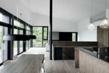 a minimalist dining space with a stained dining table, white chairs, black pendant lamps and a glazed wall for light and views