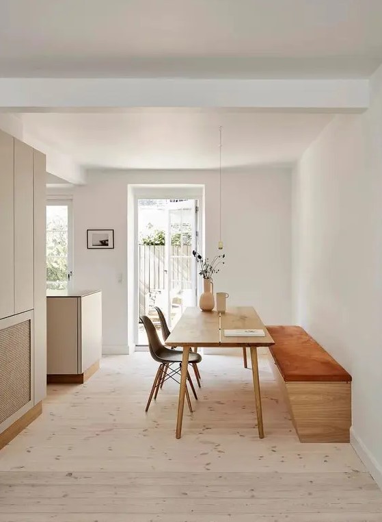 a minimalist dining space with an upholstered bench, a stained table and black Eames chairs and a pendant lamp