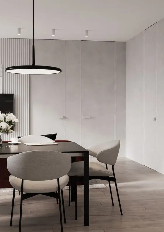 a minimalist light grey dining room with a black table, neutral chairs, a black pendant lamp is a stylish space for meals and work
