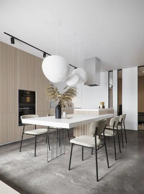 a minimalist neutral dining space with a white table, creamy chairs, a cluster of pendant lamps and a large fluted storage unit
