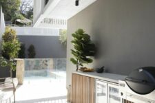 a minimalist outdoor bbq area with a grill and a fridge, with a statement plant next to it is a cool space to be in