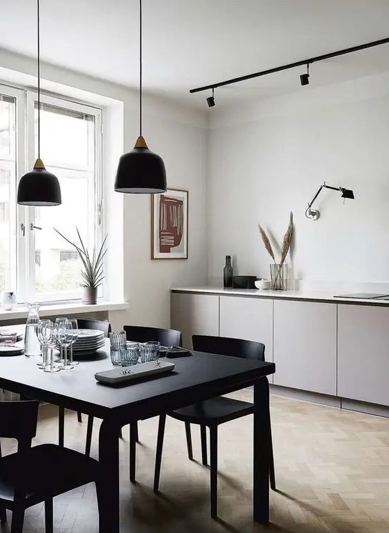 a minimalist space with sleek grey cabinets, a black table and chairs, black pendant lamps and some grasses in vases