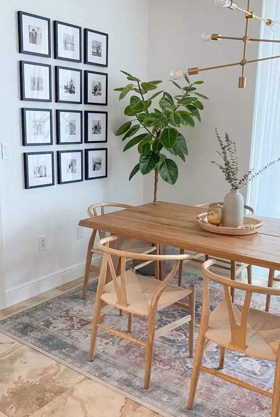 a modern Scandinavian dining space with a light-stained table and wishbone chairs, a potted plant and a grid gallery wall