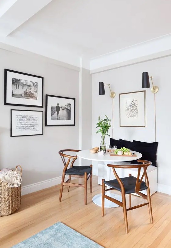 a modern dining nook with a built-in bench, a round table, stained wishbone chairs, black sconces and artworks