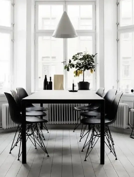a modern dining space by the window, with a black table, black Eames chairs and a white cone pendant lamp plus a lemon tree