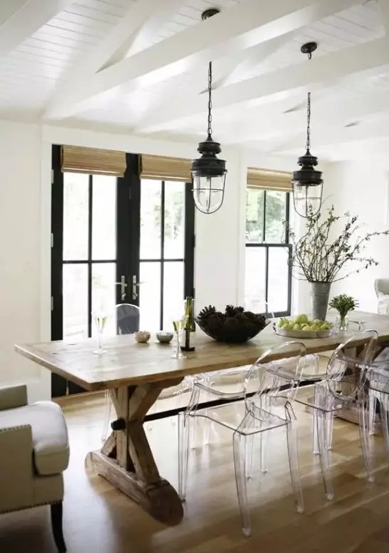 a modern farmhouse dining room with a wooden table, wicker shades, ghost chairs, vintage lanterns and black doors
