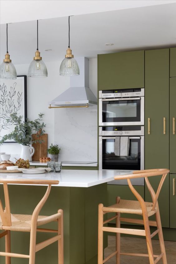 a modern farmhouse kitchen in olive green, with sleek cabinets, a matching kitchen island, Wishbone chairs and pendant lamps