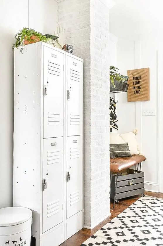 a modern farmhouse murdroom with brick walls, white lockers, a leather upholstered bench, a crate and a printed rug