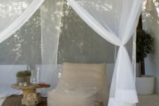 a modern neutral outdoor space with a printed soft chair, a side table and a candle lantern plus a mosquito net canopy