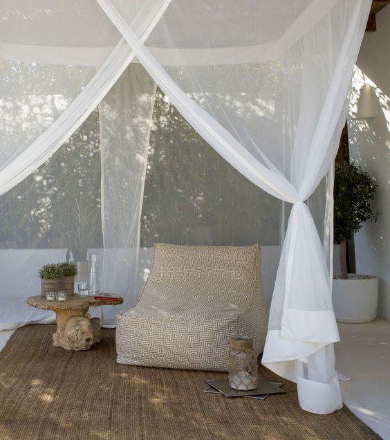 a modern neutral outdoor space with a printed soft chair, a side table and a candle lantern plus a mosquito net canopy
