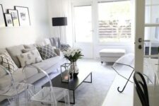 a monochromatic living room with a grey sofa, ghost chairs, a low black coffee table, a white pouf and a ledge gallery wall