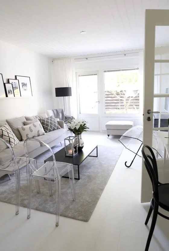 a monochromatic living room with a grey sofa, ghost chairs, a low black coffee table, a white pouf and a ledge gallery wall