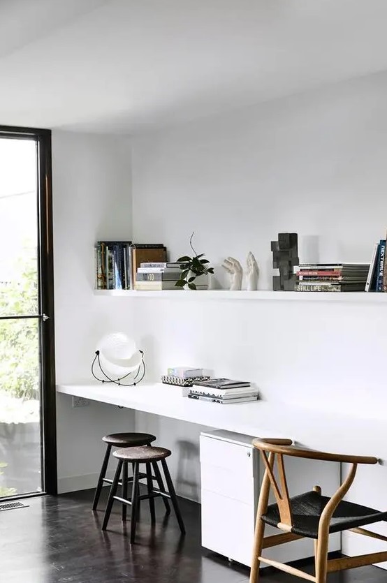 a neutral Scandinavian study and work space with a long shelf with books and decor, a shared desk, stools and a wishbone chair
