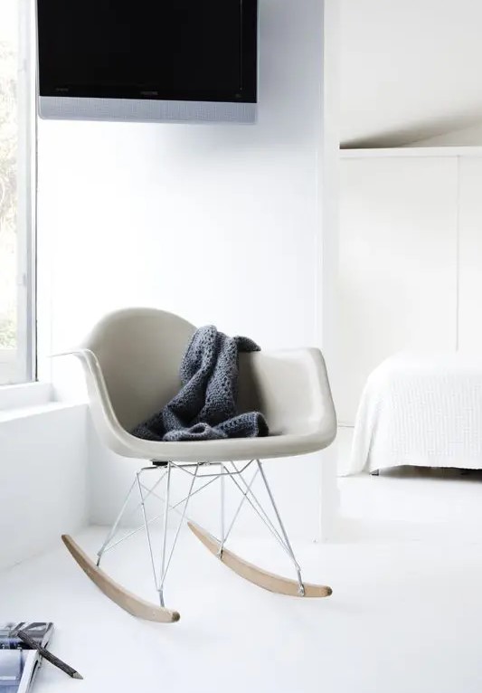 a neutral light filled space with a grey Eames rocker, a white bed and bedding, a built in cabinet for storage