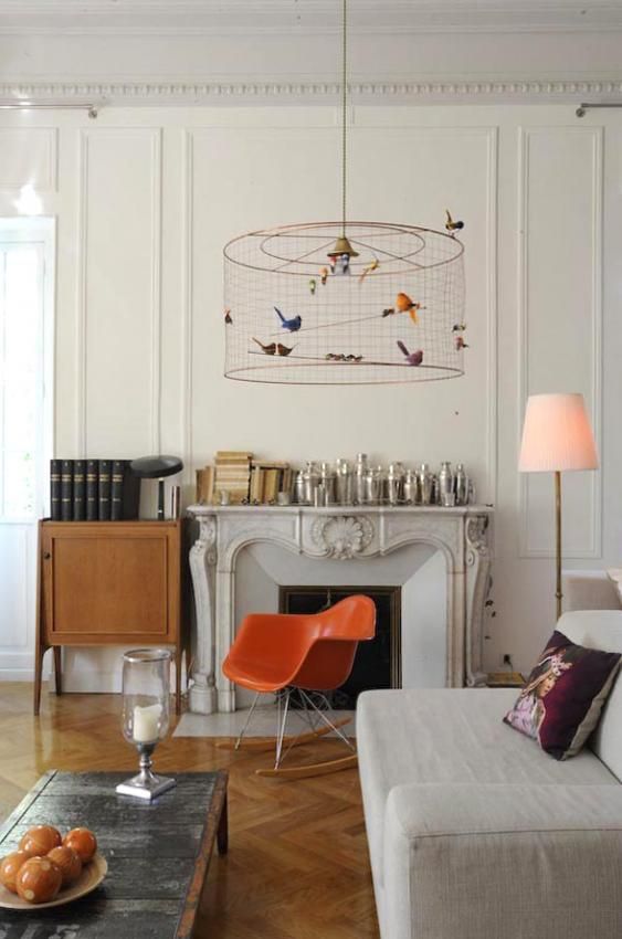 a neutral living room with a vintage fireplace, a neutral sofa, an orange Eames chair, a floor lamp and a cage-style pendant lamp