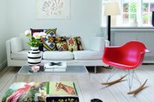 a neutral living room with a white sofa, a colorful ottoman, a bold fuchsia Eames chair, printed pillows and an artwork
