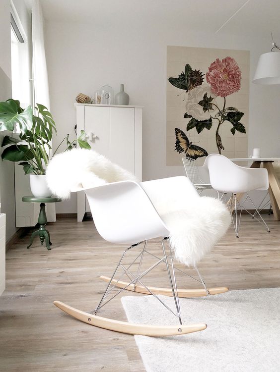 a neutral space with a white Eames rocker, white chairs, a white storage unit and a botanical artwork plus some potted plants