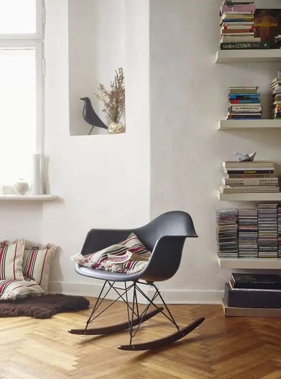 a reading nook by the window, with bookshelves, a grey Eames rocker and some pillows right on the floor
